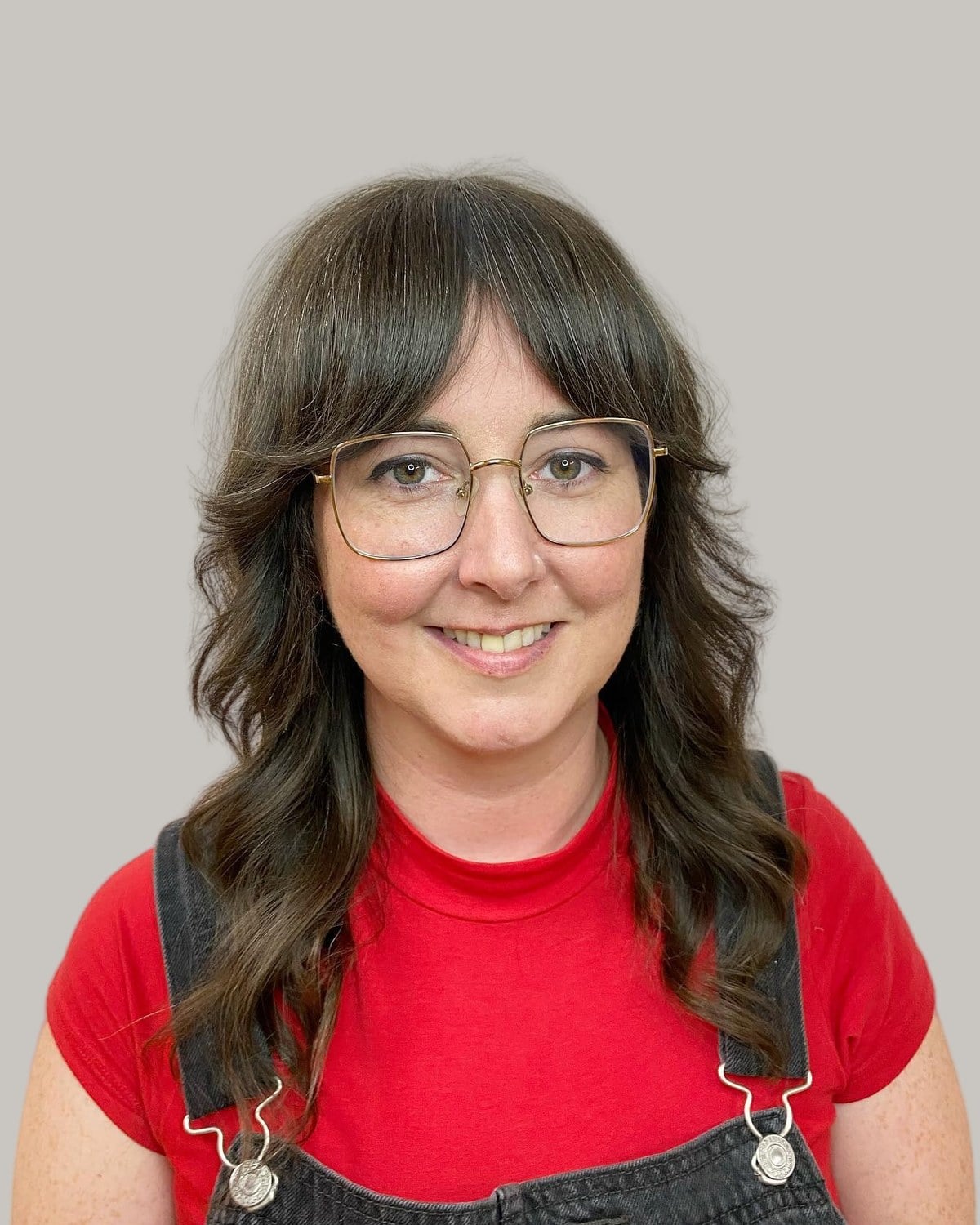 Smiling woman with long dark waves, curtain bangs and glasses