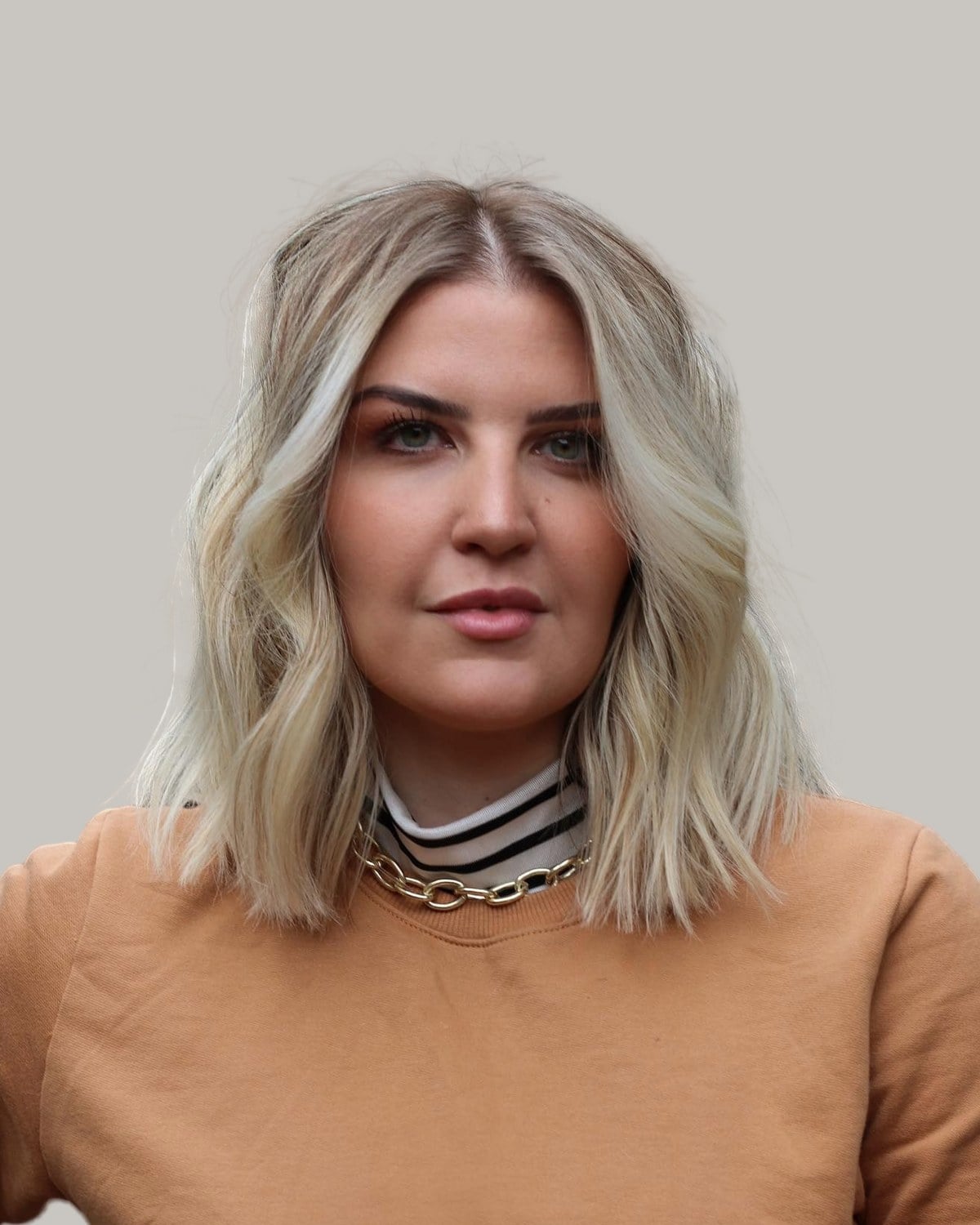 Woman with a blonde lob and soft waves, in a camel sweater