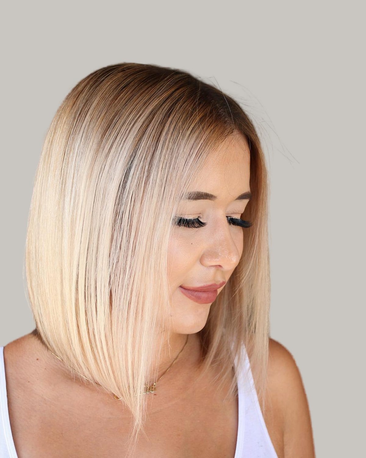 Woman with a sleek, honey-blonde lob with a dark root, seen in three-quarter view