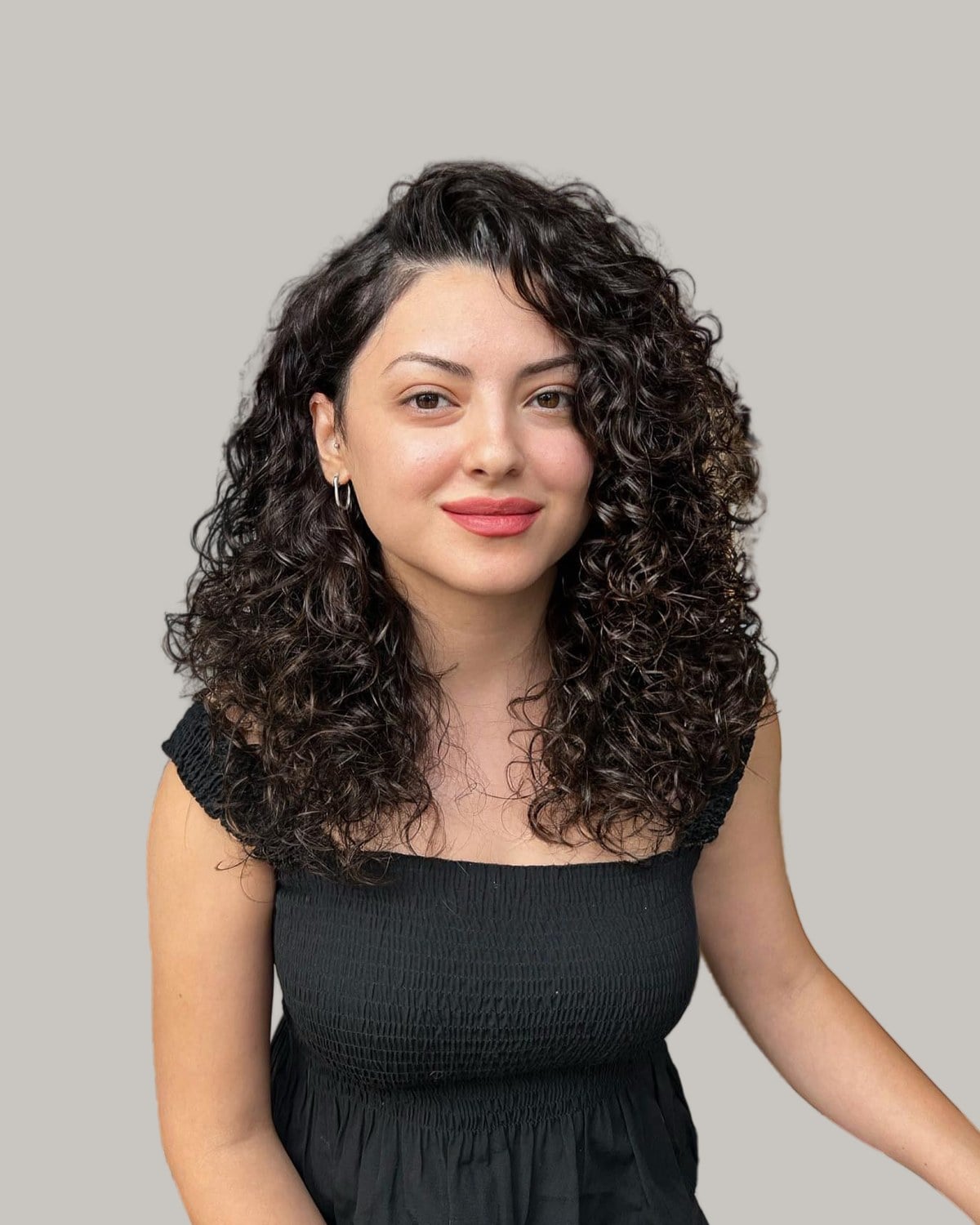 Smiling woman with long, dark curls and a side part, in a black top
