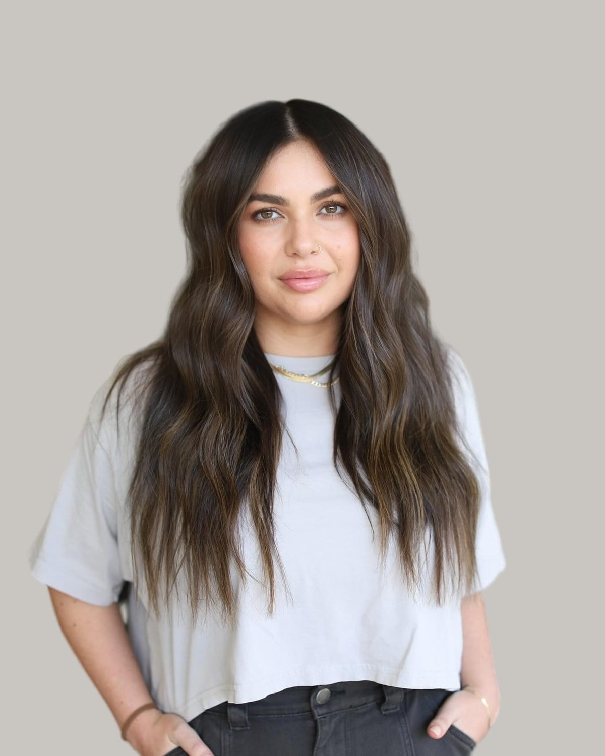 Woman with long, dark-brown waves and a center part, in a cropped T-shirt