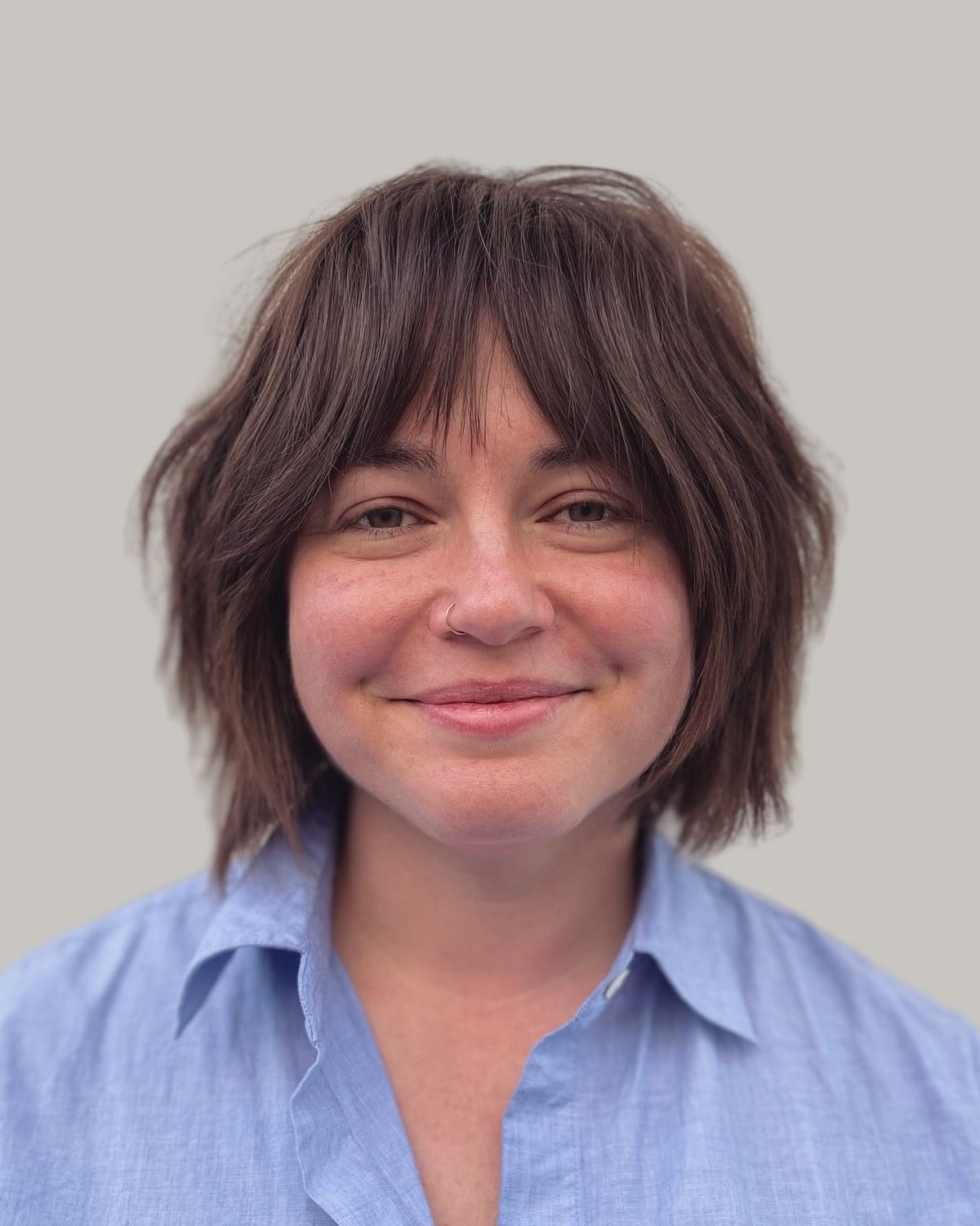 Smiling woman with a brown shaggy bob and wispy bangs, in a blue shirt