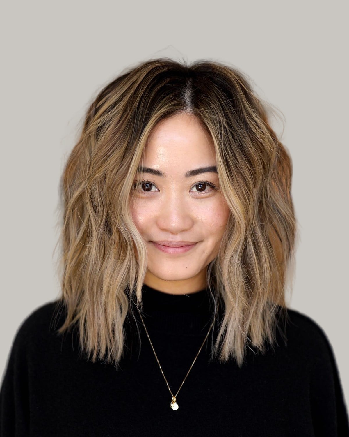 Woman with shoulder-length, highlighted waves and a center part, in a black sweater