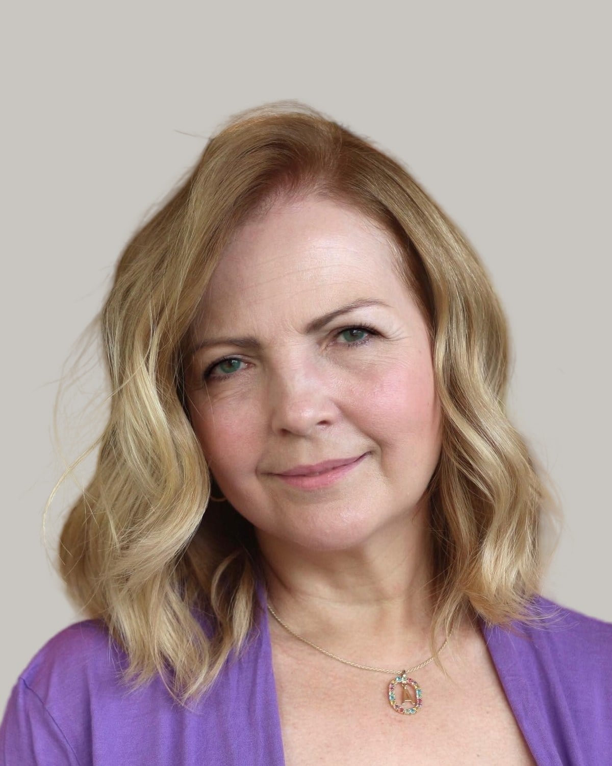 Smiling woman with a wavy blonde lob and a side part, in a purple cardigan