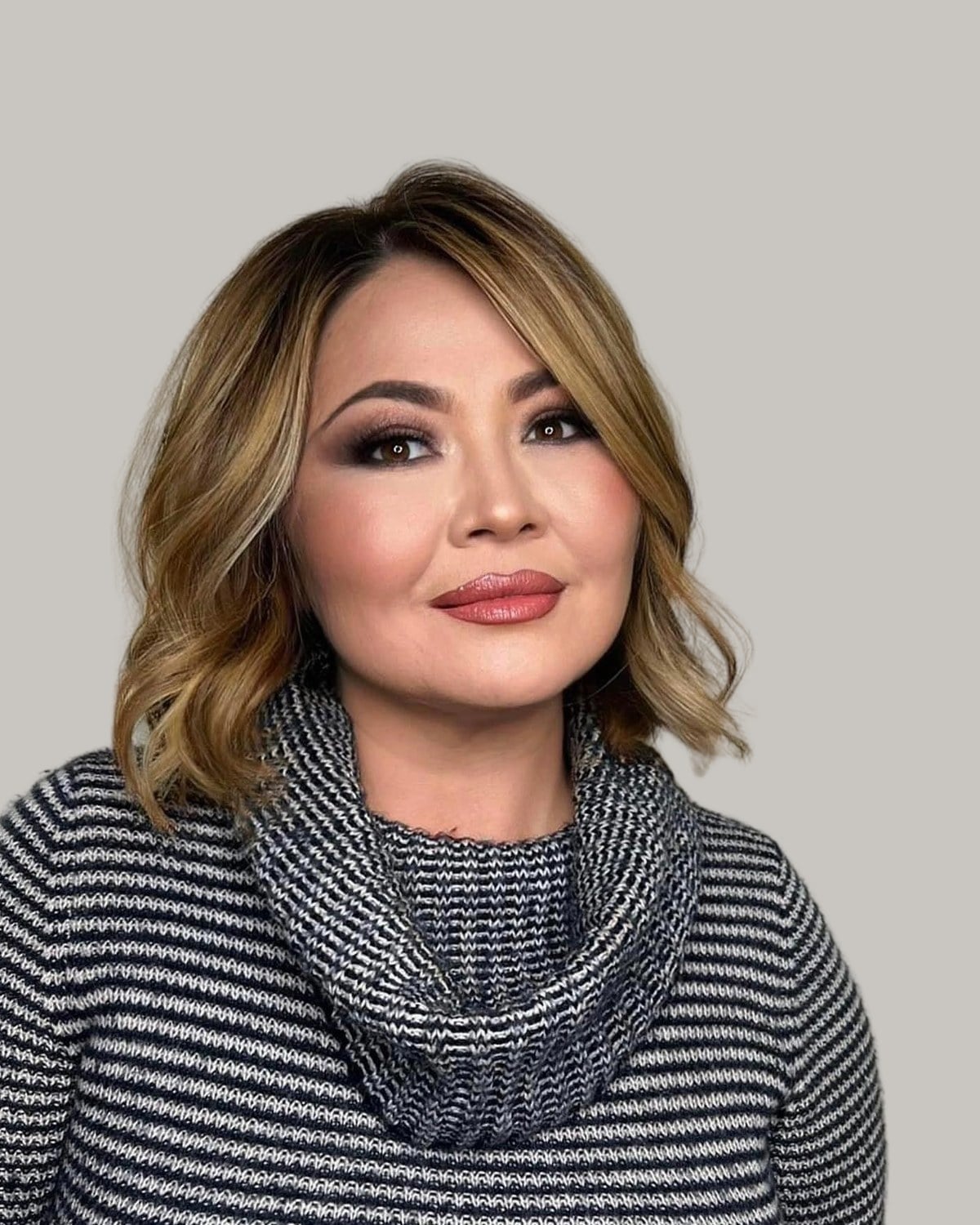 Woman with a honey-blonde lob in soft waves, in a striped turtleneck