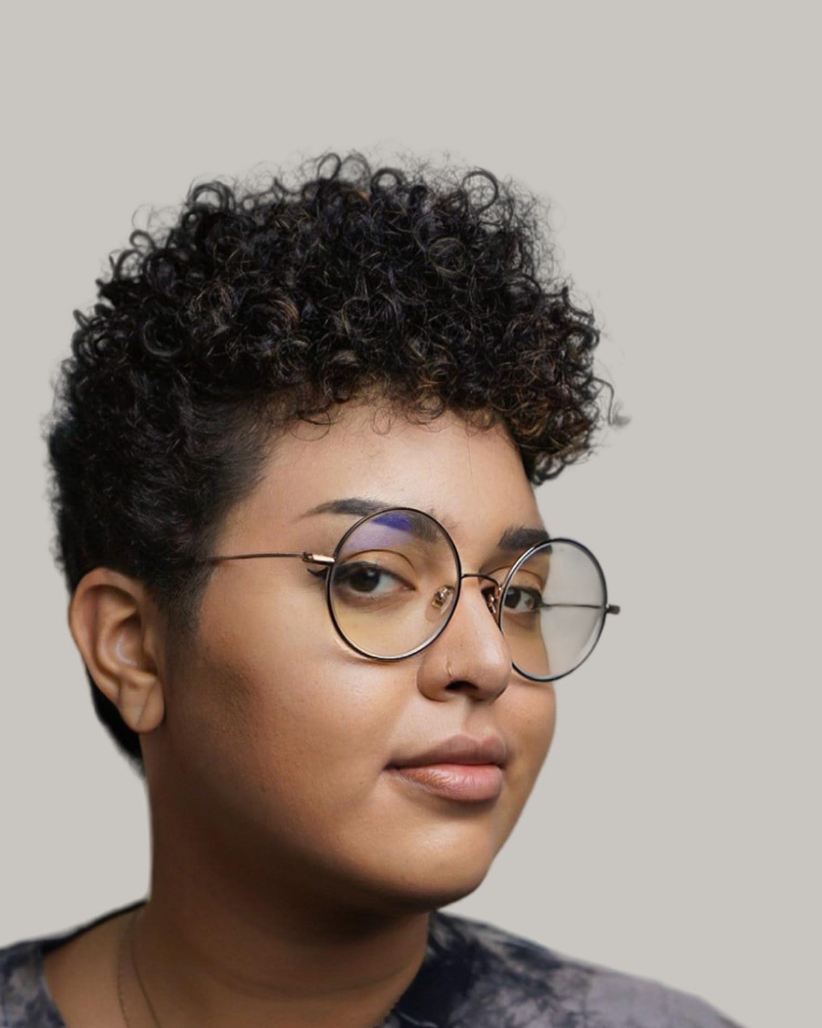 Woman with a tapered natural cut and round glasses, seen in three-quarter view