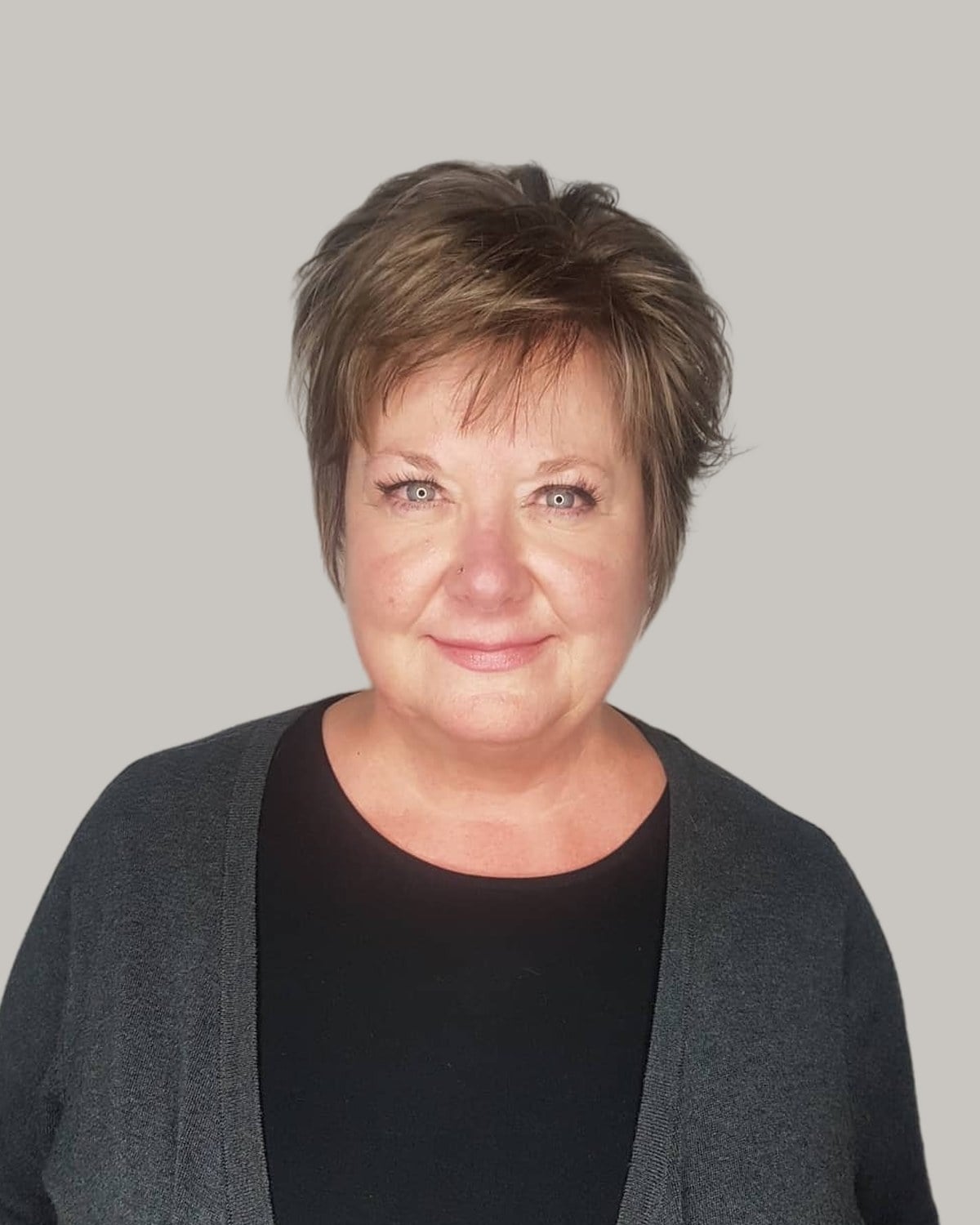Woman with a short, layered ash-brown pixie, in a gray cardigan