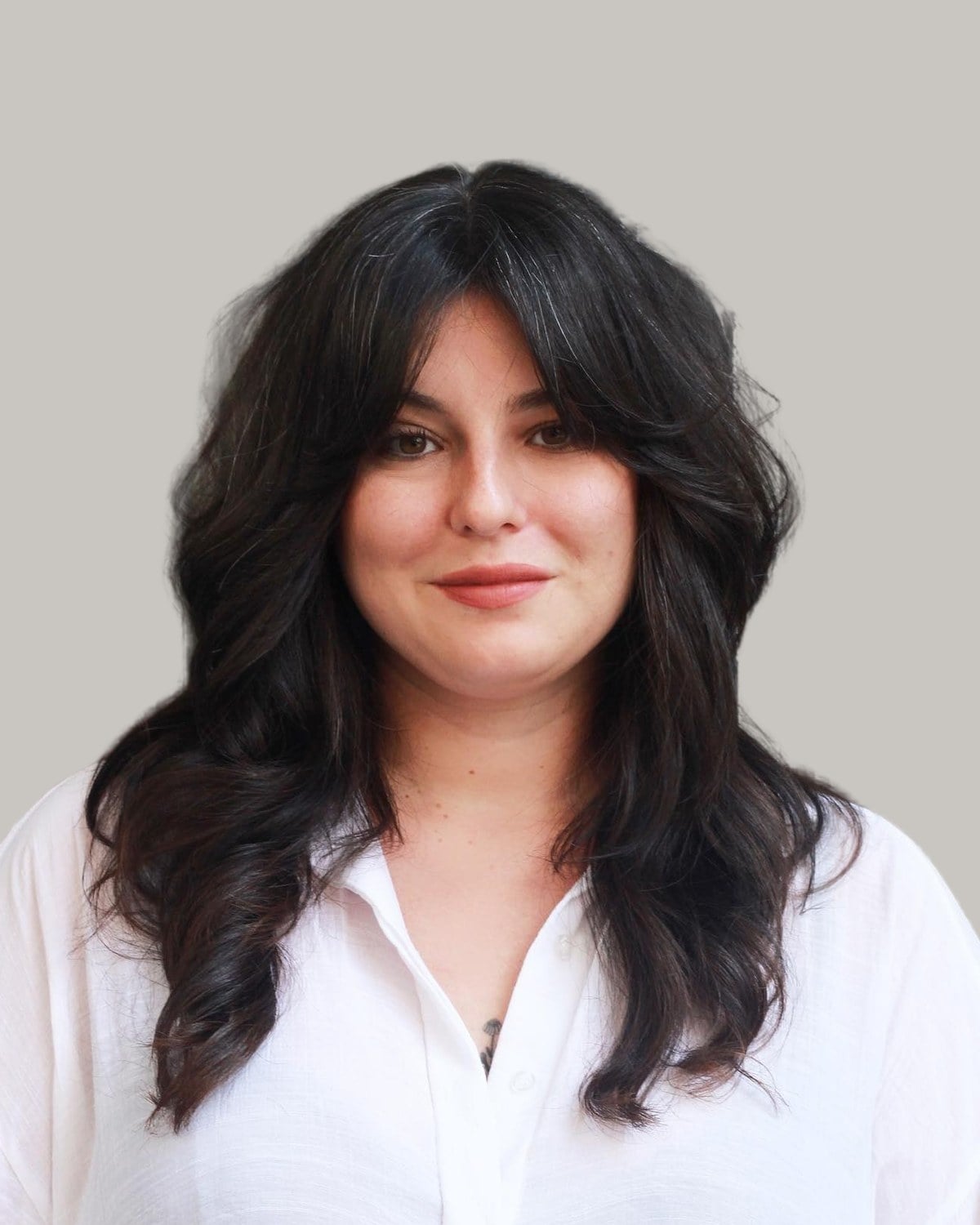 Woman with thick, dark, long layers and curtain bangs, in a white shirt
