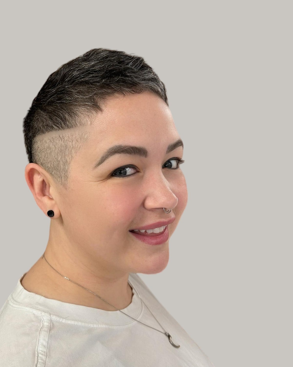 Smiling woman with a short pixie and an undercut on one side, seen in three-quarter view