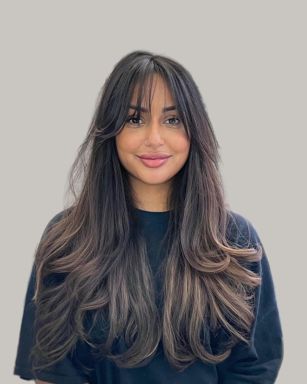 Smiling woman with long, dark layered hair and wispy bangs