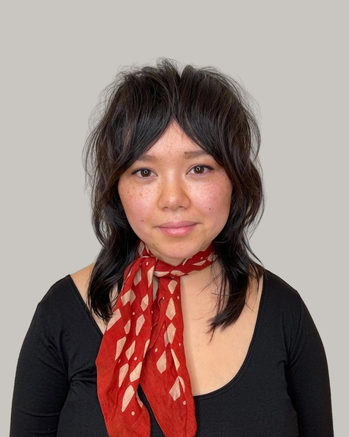 Woman with a dark wolf cut, curtain bangs and a red scarf