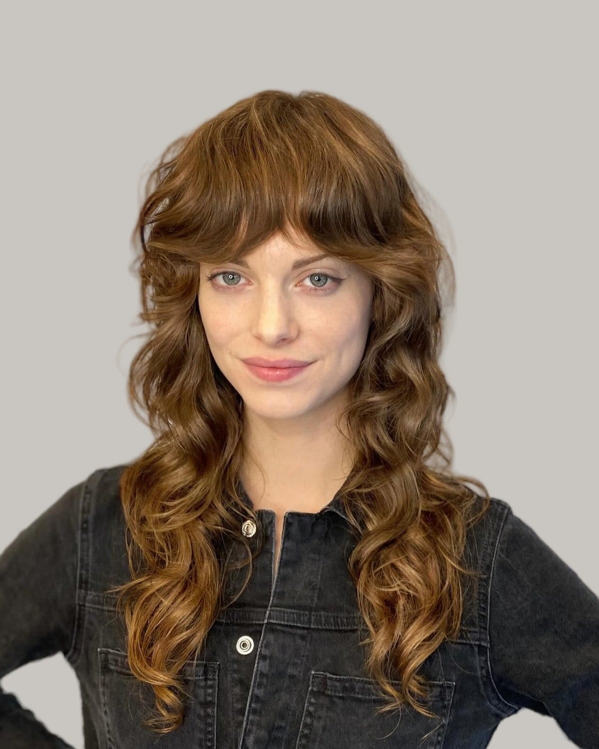 Woman with long auburn curls and long, tousled bangs, in a denim jacket