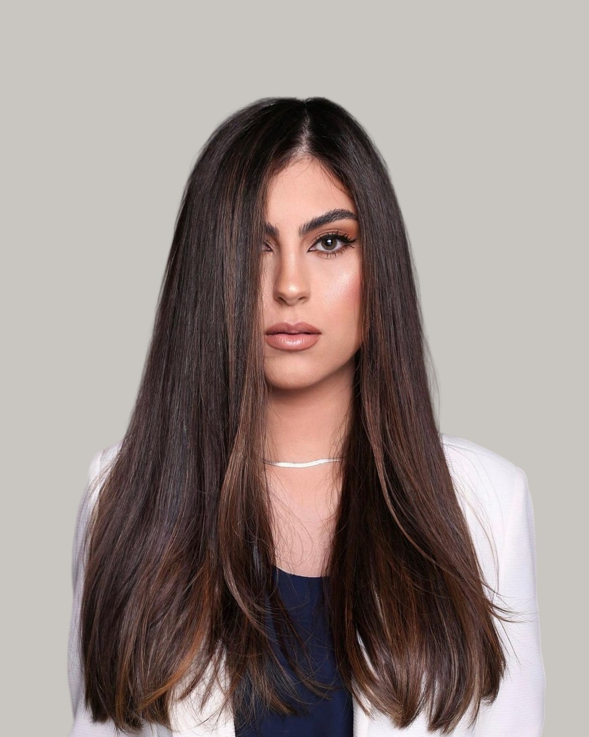 Woman with long, straight dark-brown hair and a center part, in a white blazer