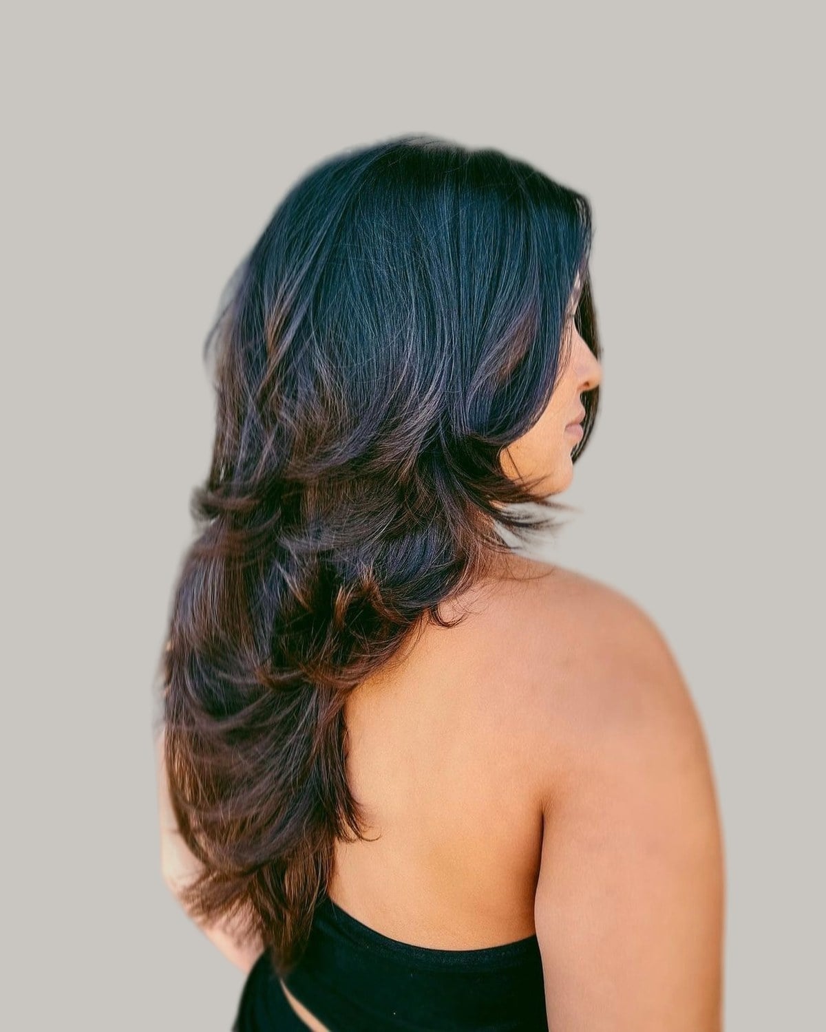 Woman with long dark-brown layered hair, seen from behind in three-quarter view
