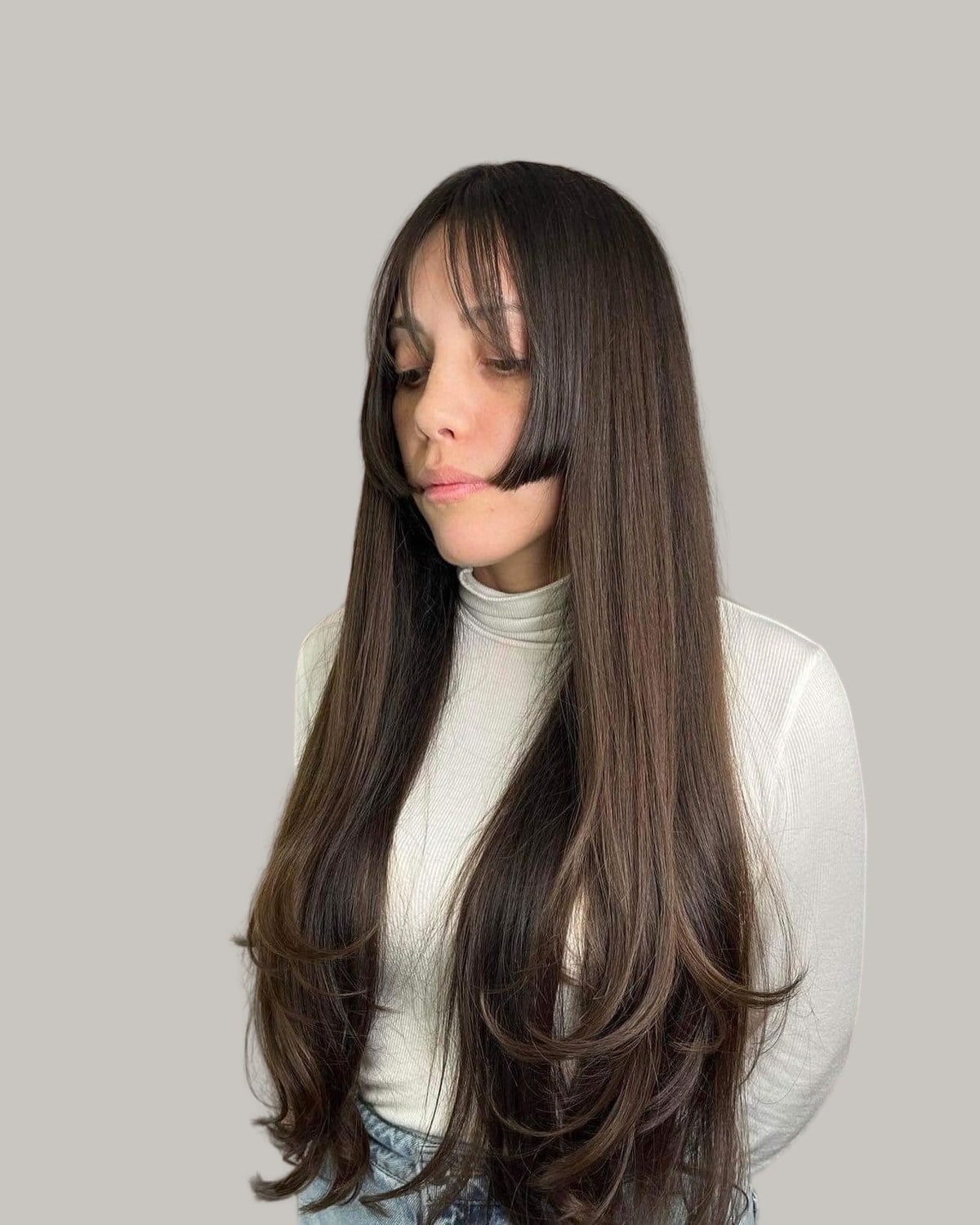 Woman with long dark-brown hair, bangs and jaw-length side panels, looking down