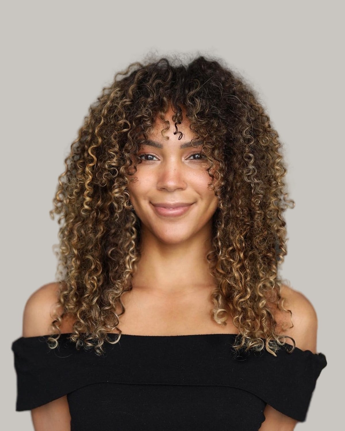 Smiling woman with long highlighted curls and curly bangs