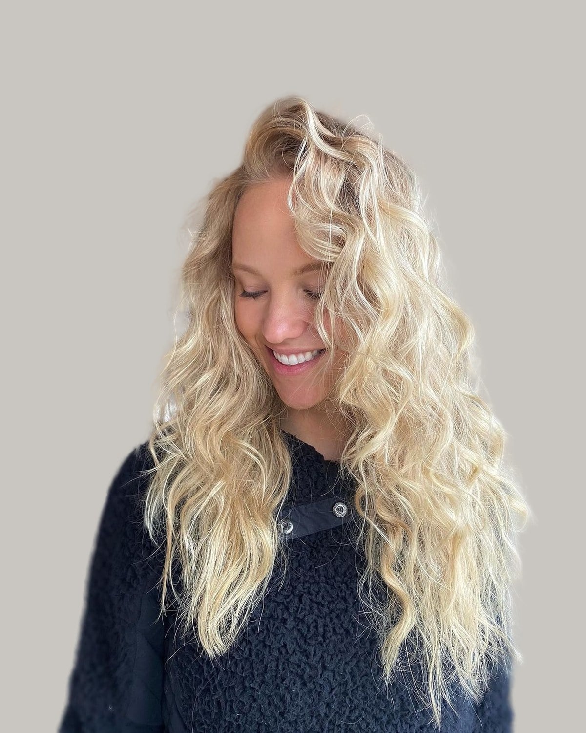 Smiling woman with long, platinum-blonde curls, looking down