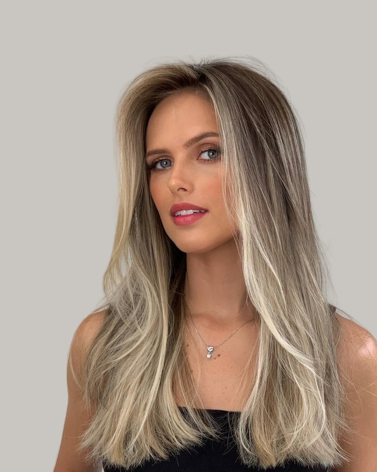 Woman with long, fine, straight blonde hair with dark roots, looking to the side