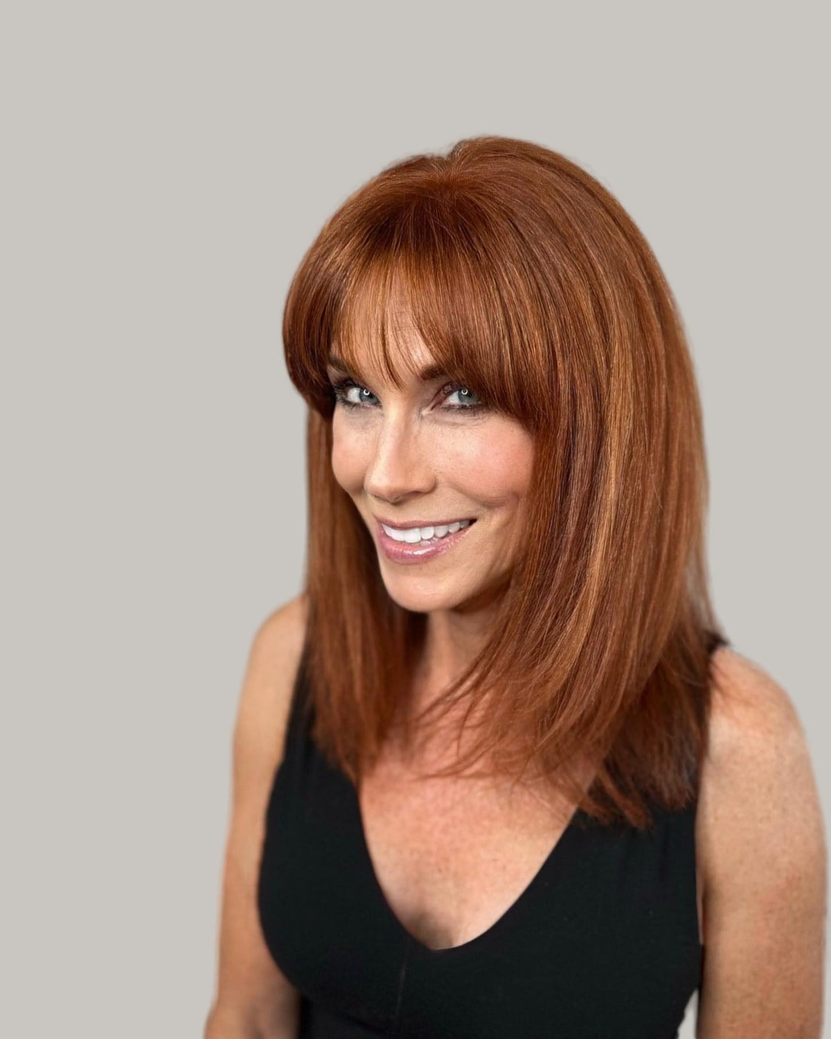 Smiling older woman with long copper-red hair and full blunt bangs