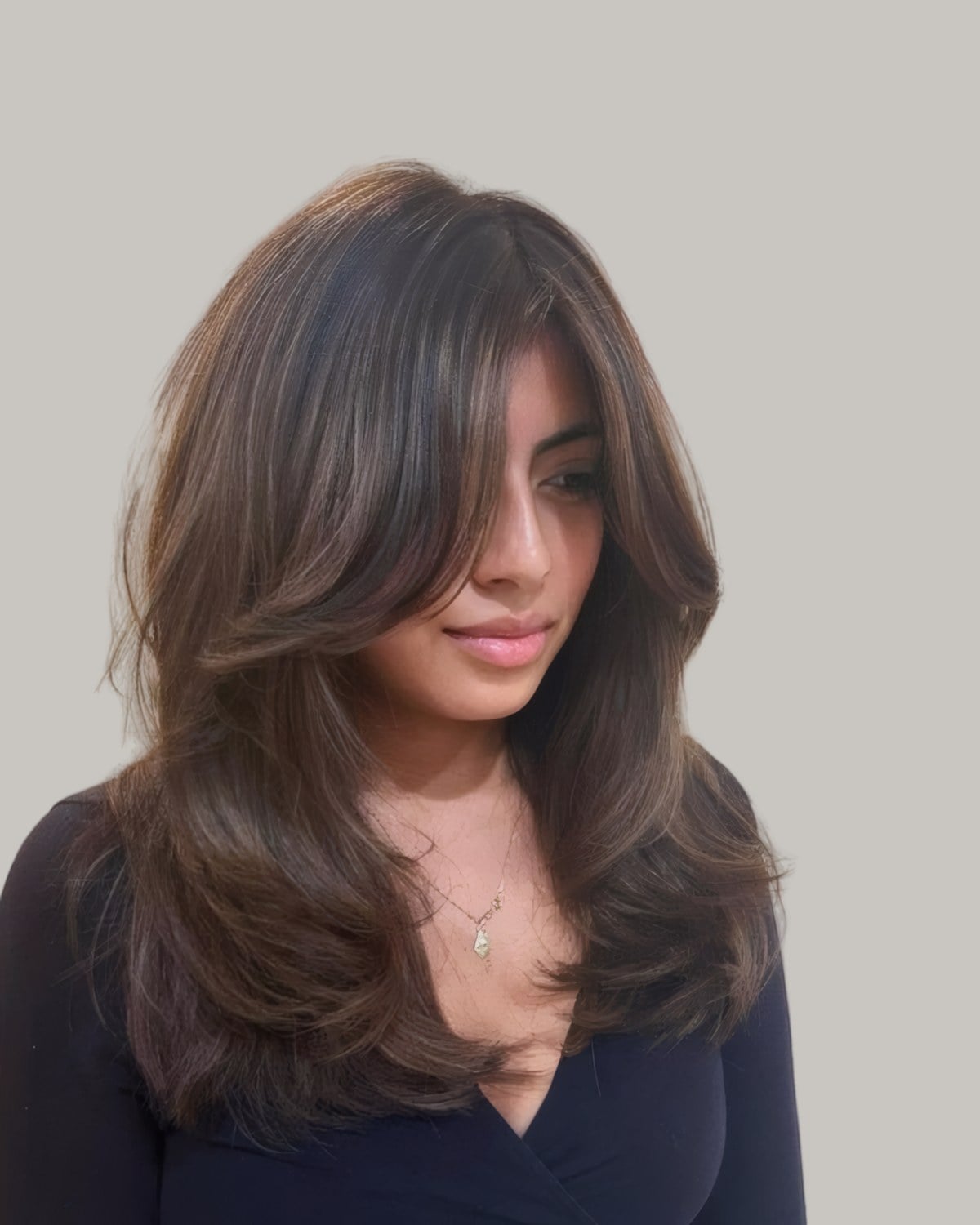 Woman with long dark-brown layers and long bangs swept to one side, looking down