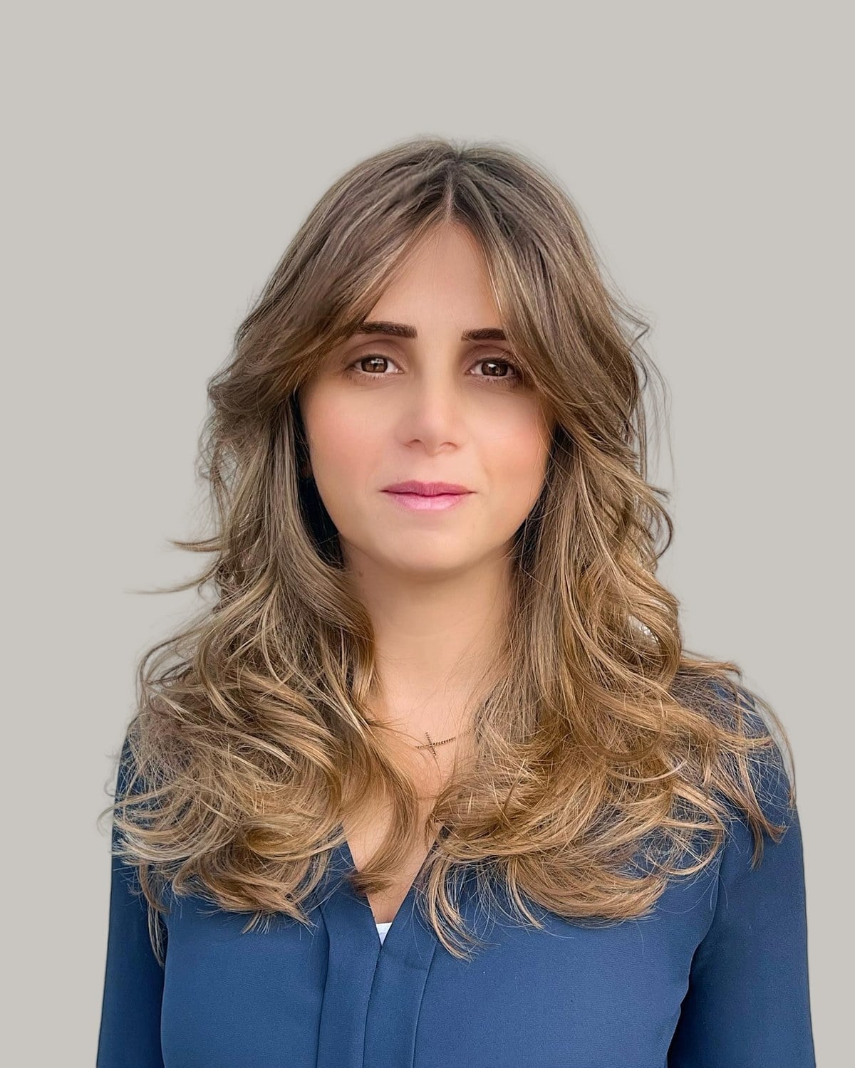 Woman with long, wavy light-brown layers and curtain bangs, in a blue blouse