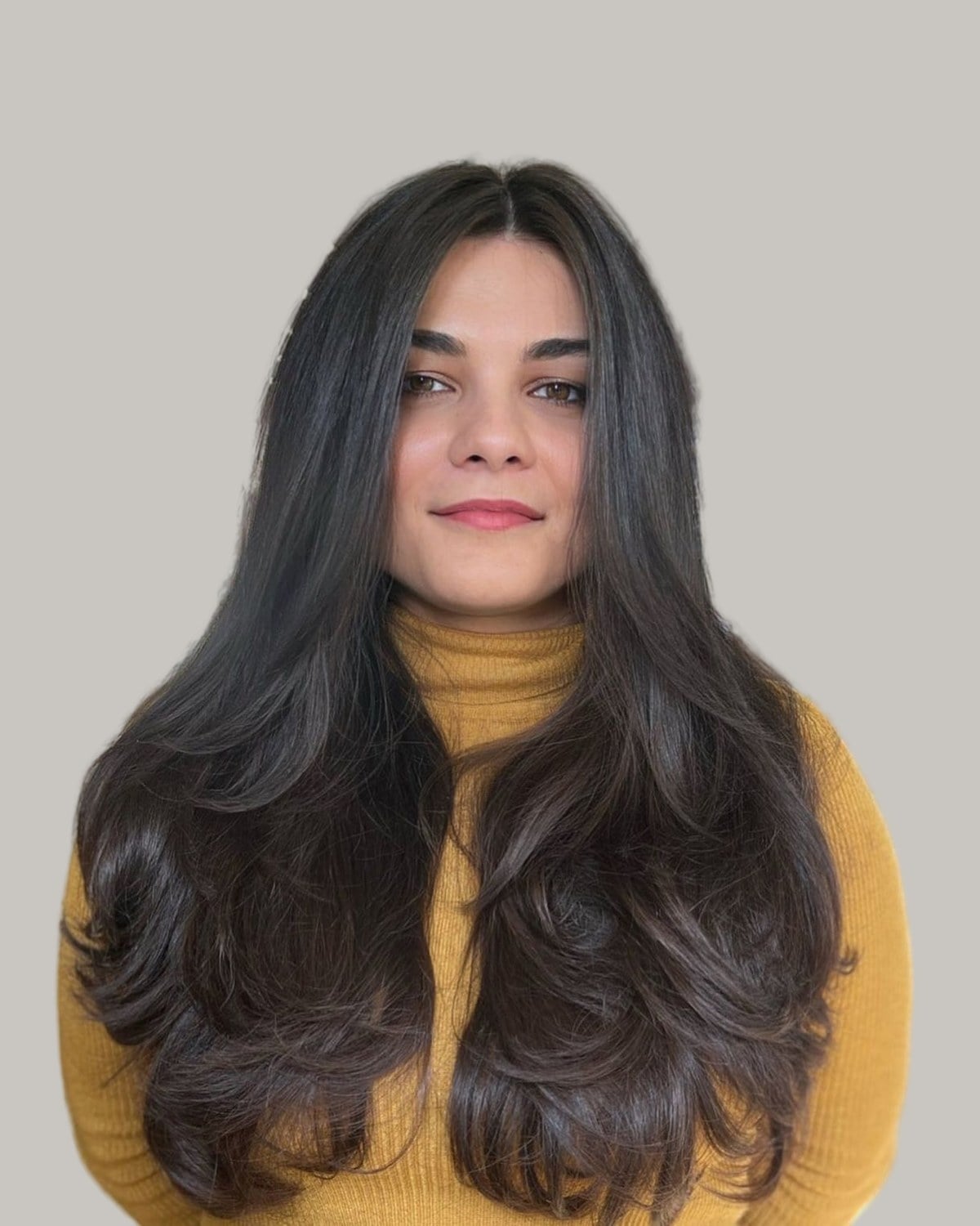 Woman with long, thick black hair and layers that flip at the ends, in a mustard sweater
