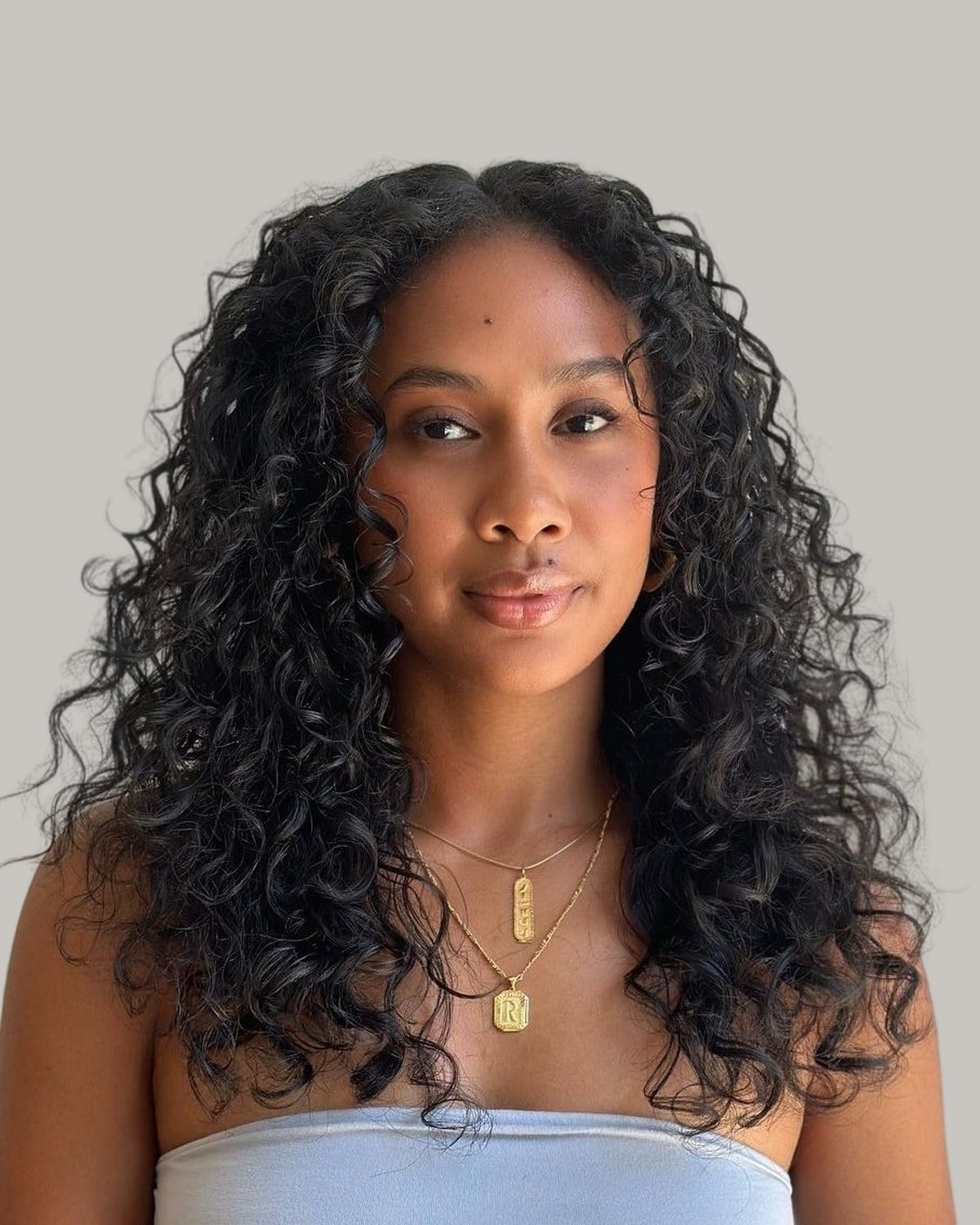 Woman with long, black natural curls and a center part, in a strapless top