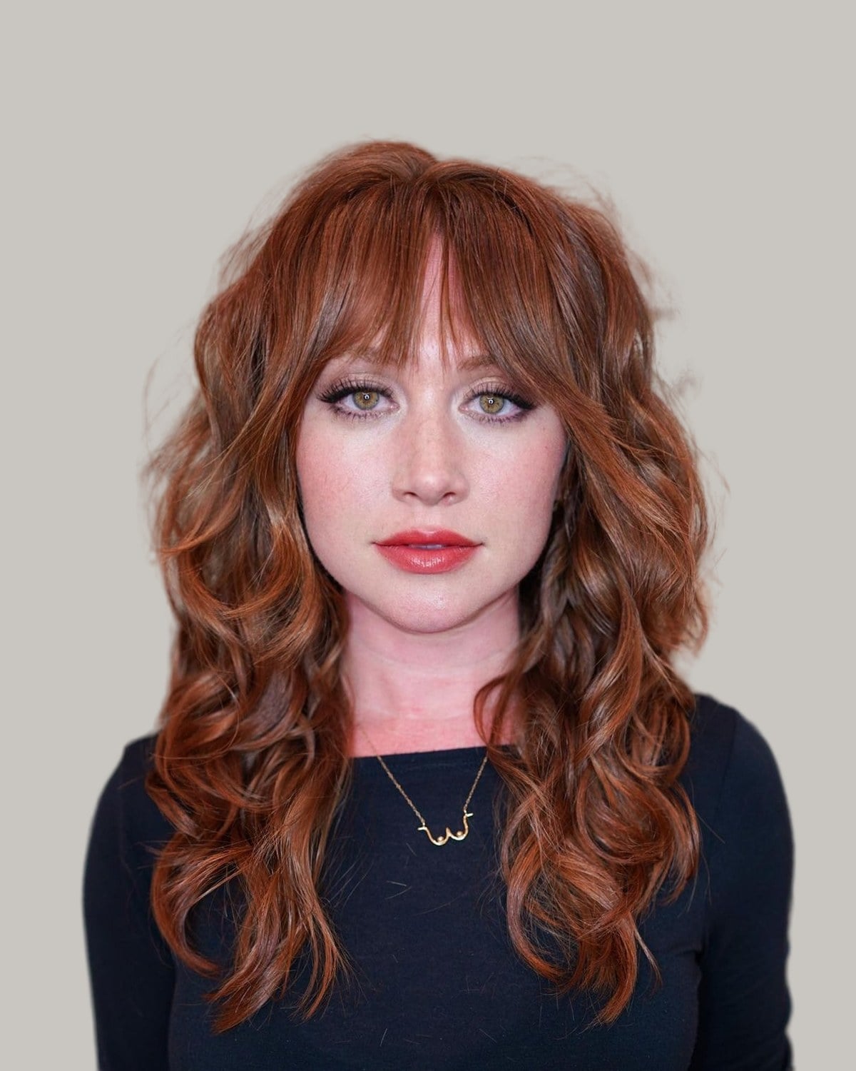 Woman with a long copper wolf cut, curtain bangs and loose curls