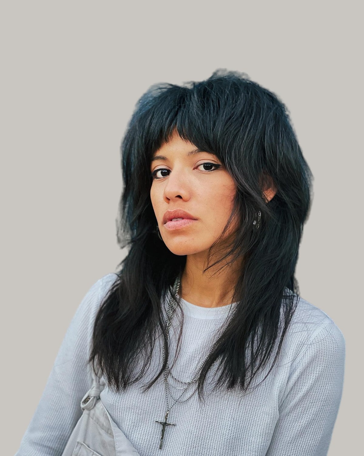 Woman with a long black wolf cut and bangs, in a gray sweater