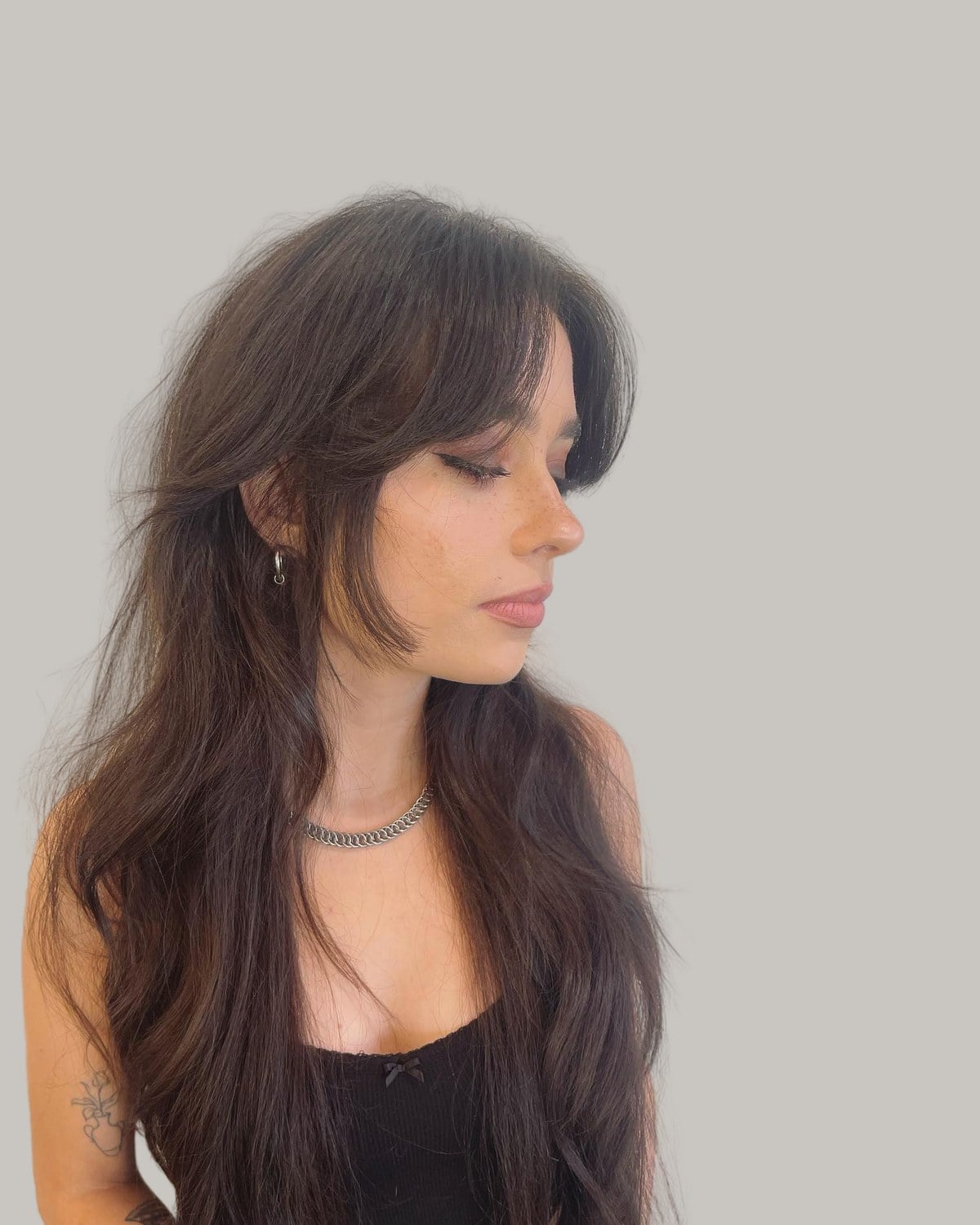 Woman with a long brown wolf cut and curtain bangs, looking to one side