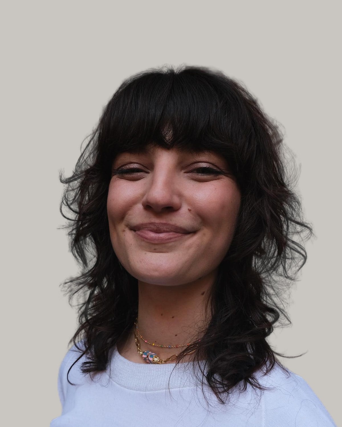 Smiling woman with a dark wavy wolf cut and full bangs, in a white sweatshirt