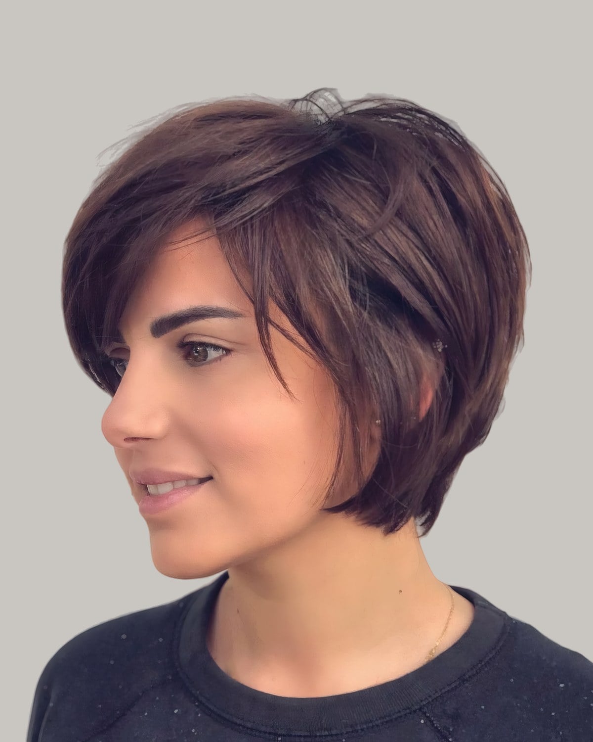 Woman with a burgundy-brown bixie and a long side fringe, smiling over her shoulder