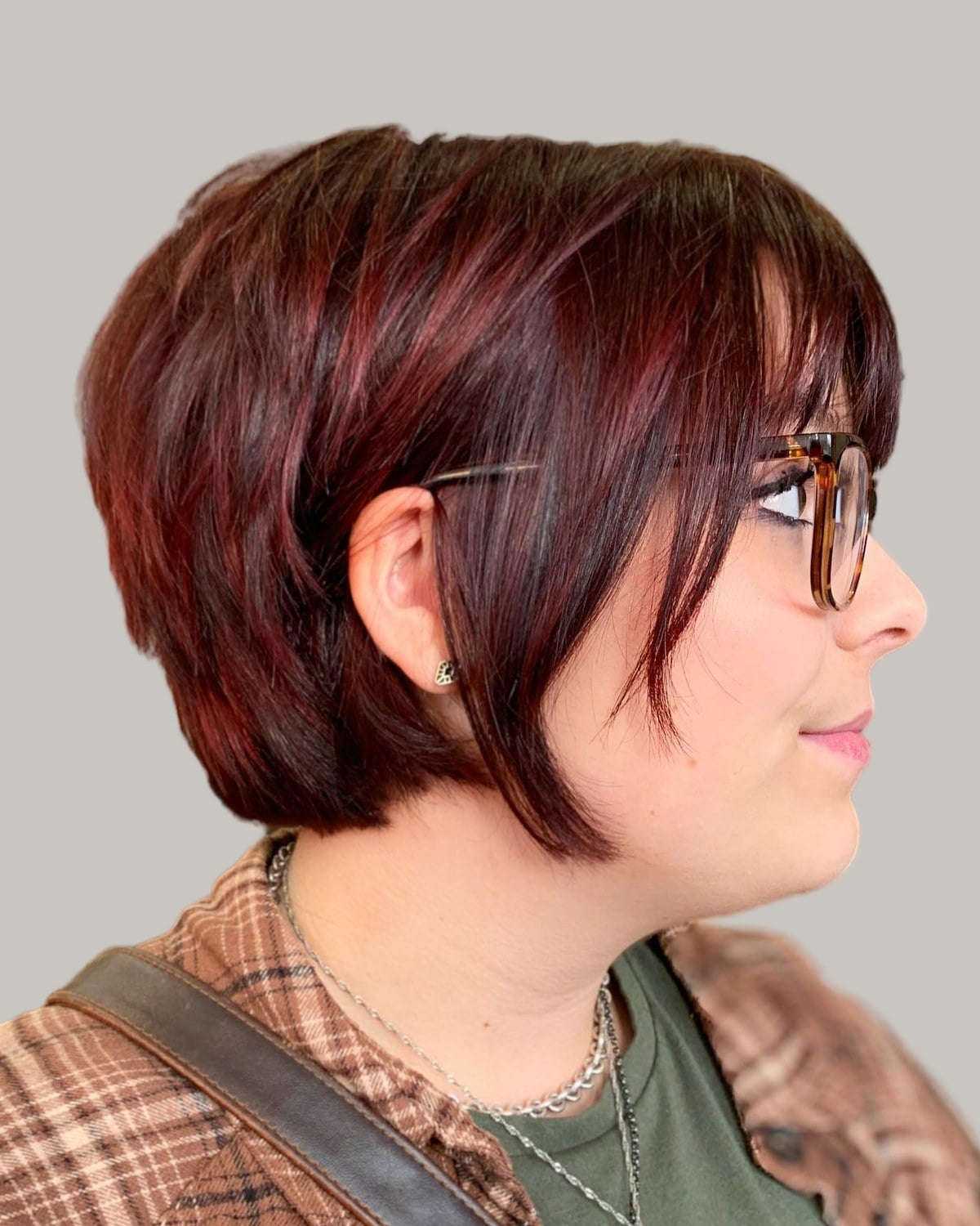 Woman in glasses with a burgundy bixie and full bangs, seen in profile