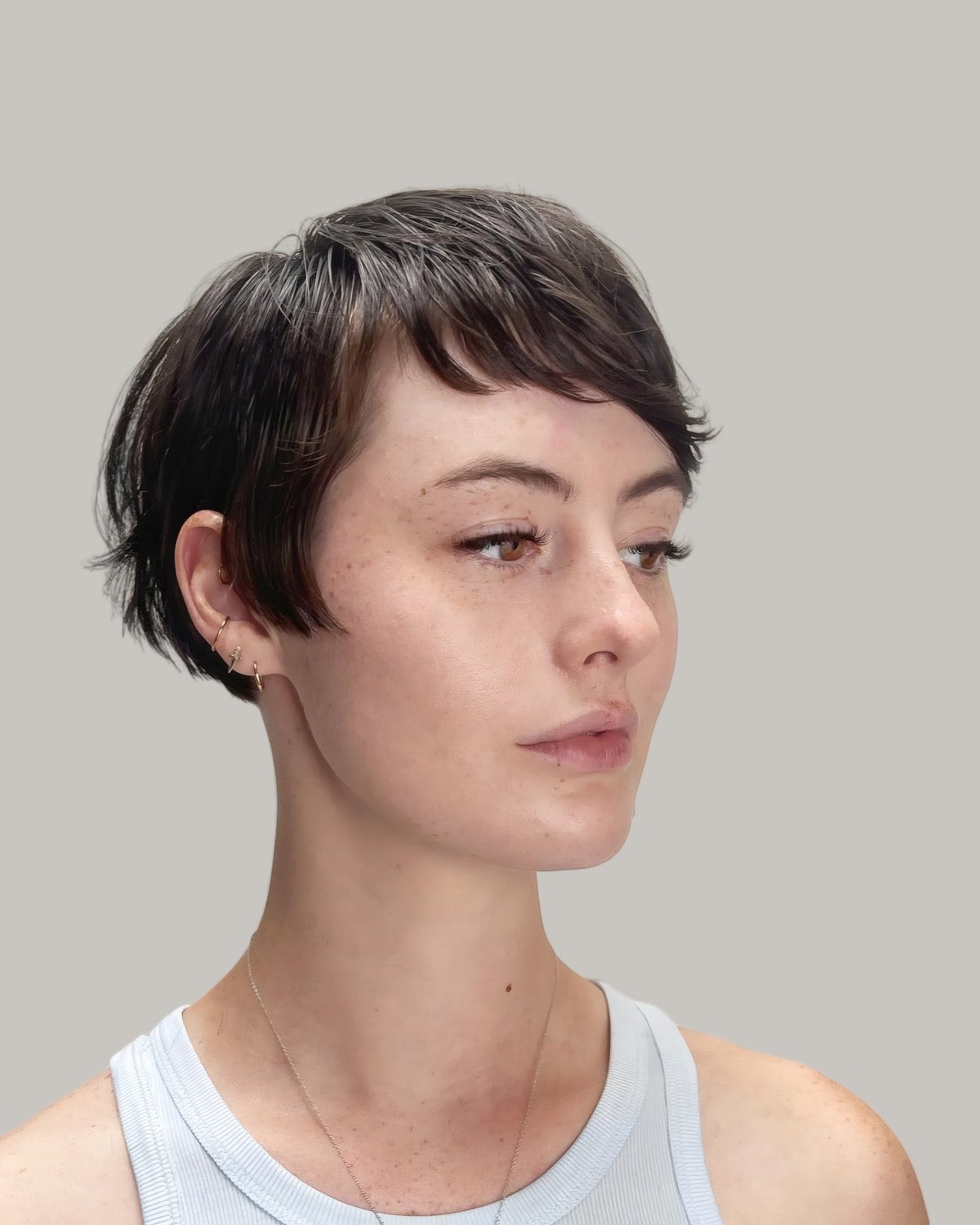 Woman with a dark-brown bixie and wispy side bangs, in a white tank top