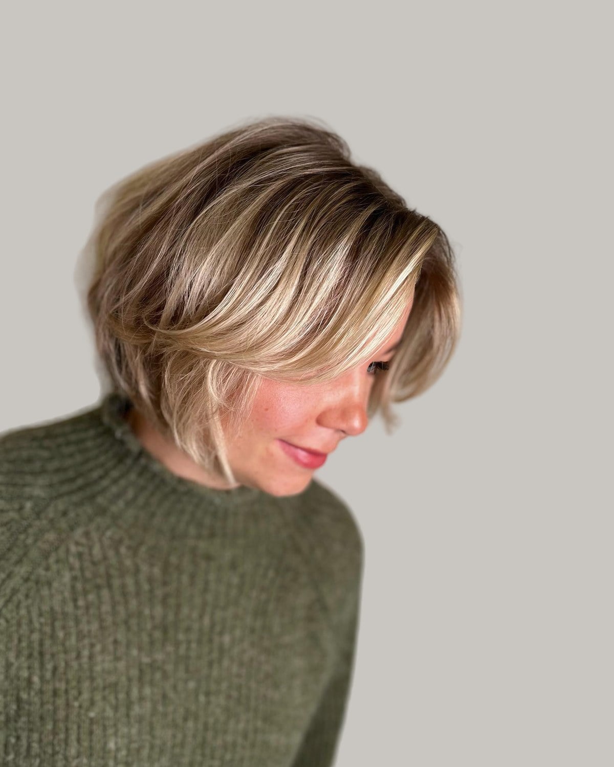 Woman with a brown bixie with blonde highlights, looking down to one side