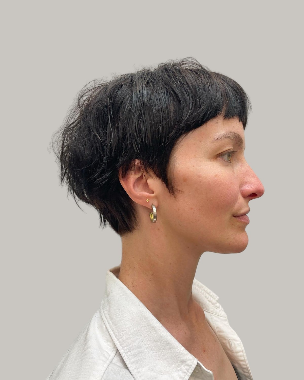 Woman in a white shirt with a black choppy bixie and a short blunt fringe, seen in profile