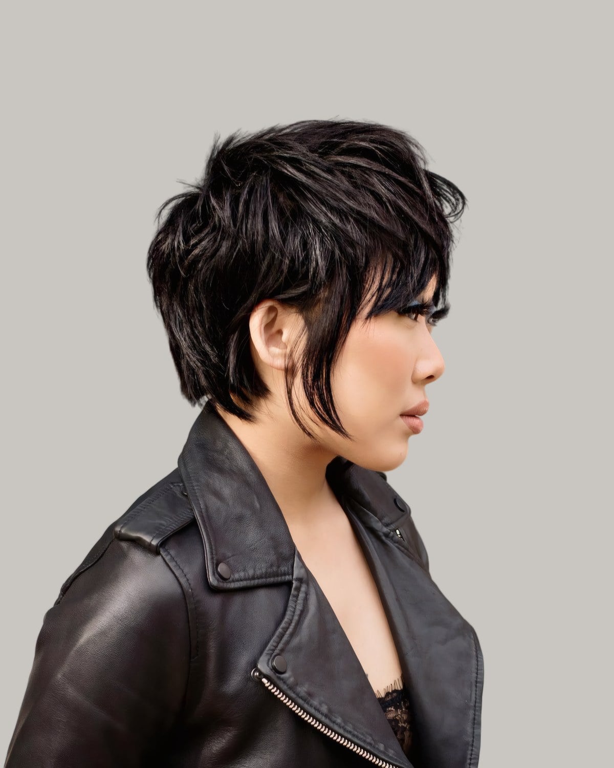 Woman in a leather jacket with a black choppy bixie, seen in profile