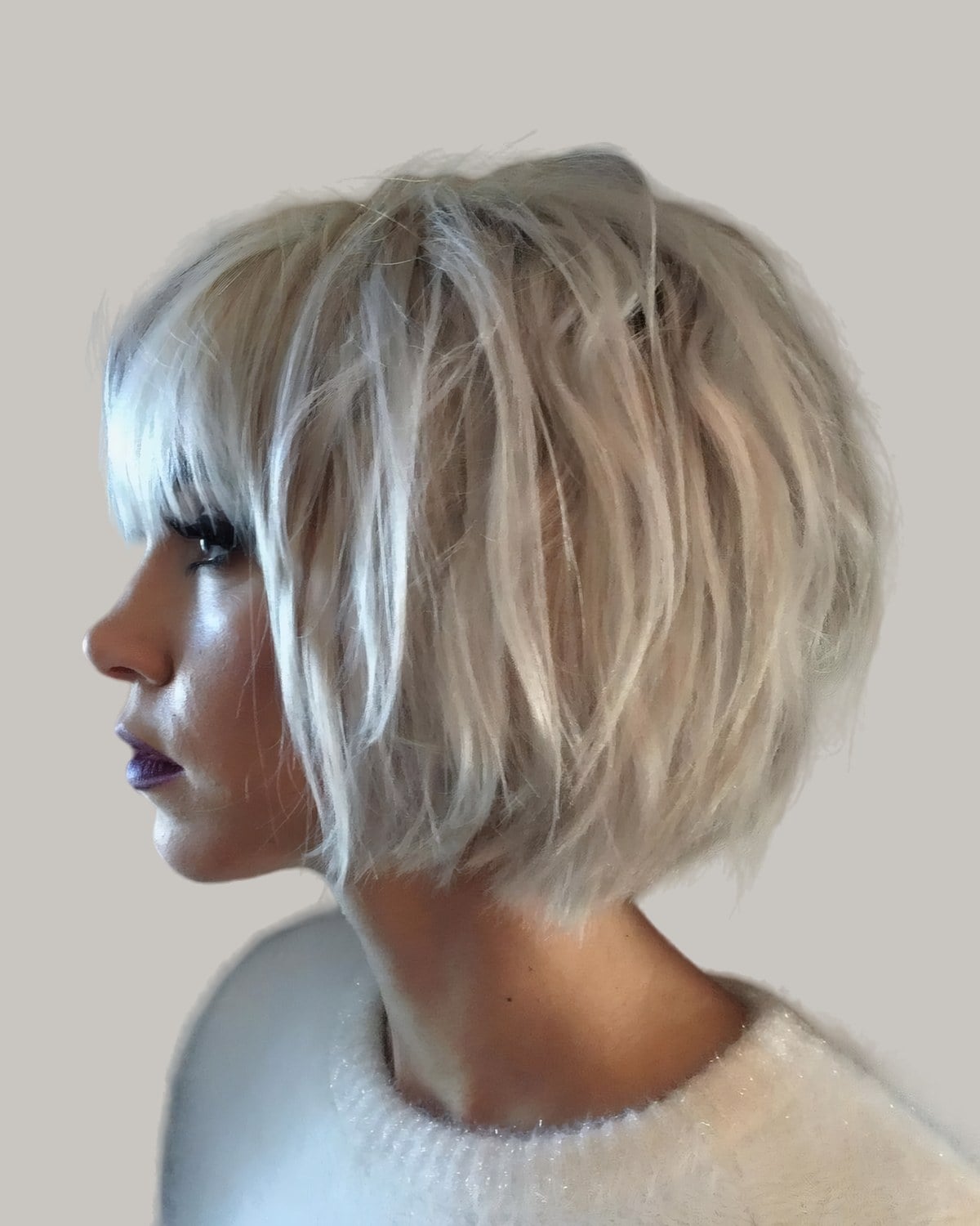 Woman with a messy platinum bob and bangs, in profile