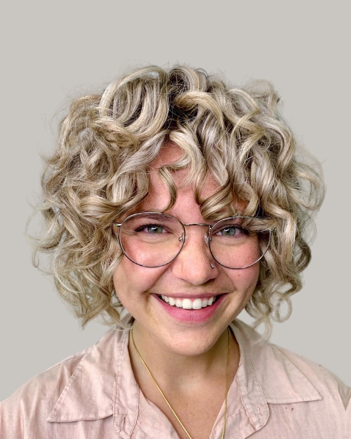 Smiling woman with blonde curls, curly bangs and round glasses