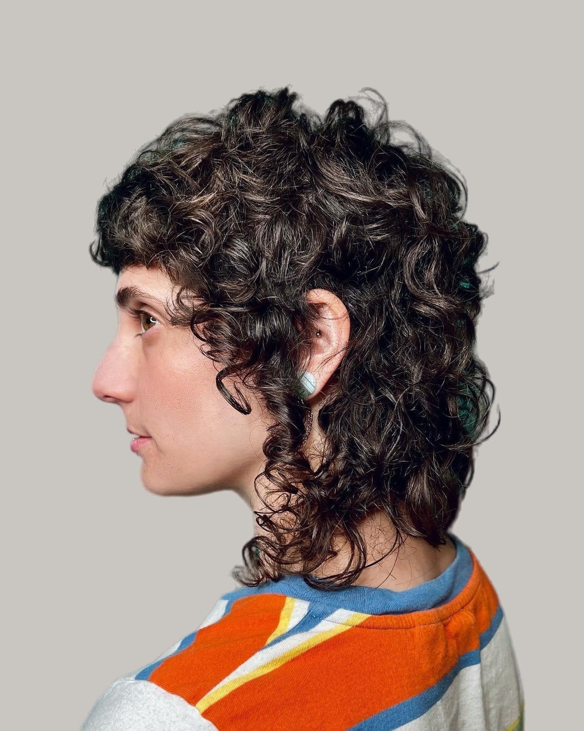Woman with a curly wolf cut and curly bangs, in profile