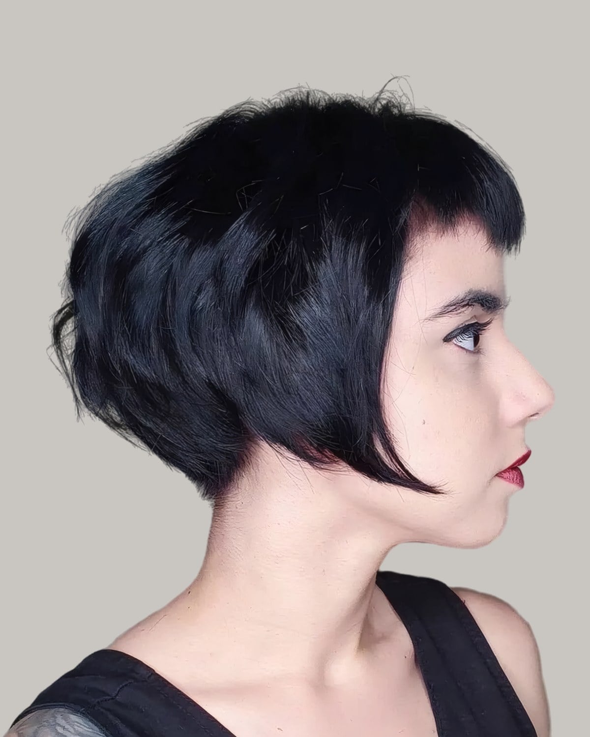 Woman with a black French bob and short blunt bangs, in profile