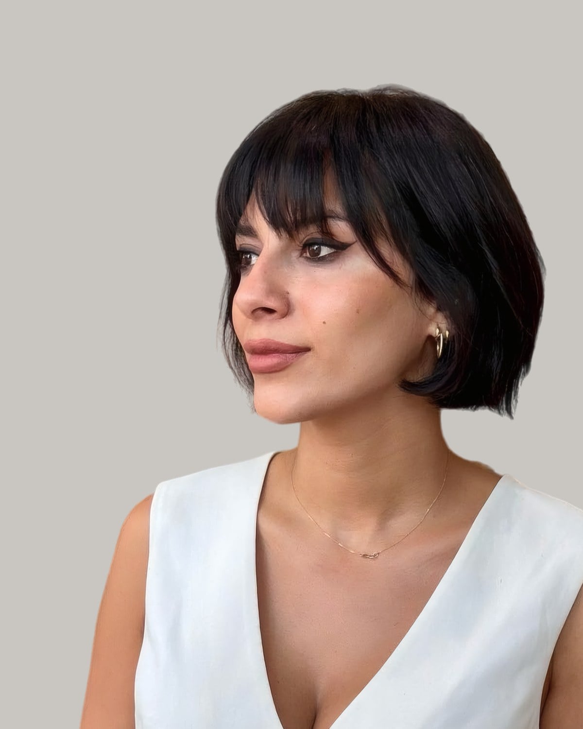 Woman with a black French bob and full bangs, turned to the side