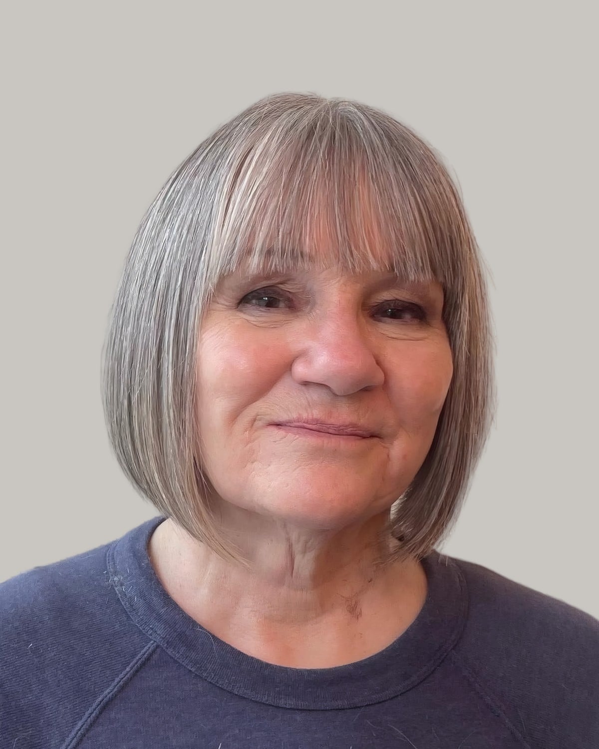Smiling woman with a straight gray bob and heavy bangs, in a navy sweater