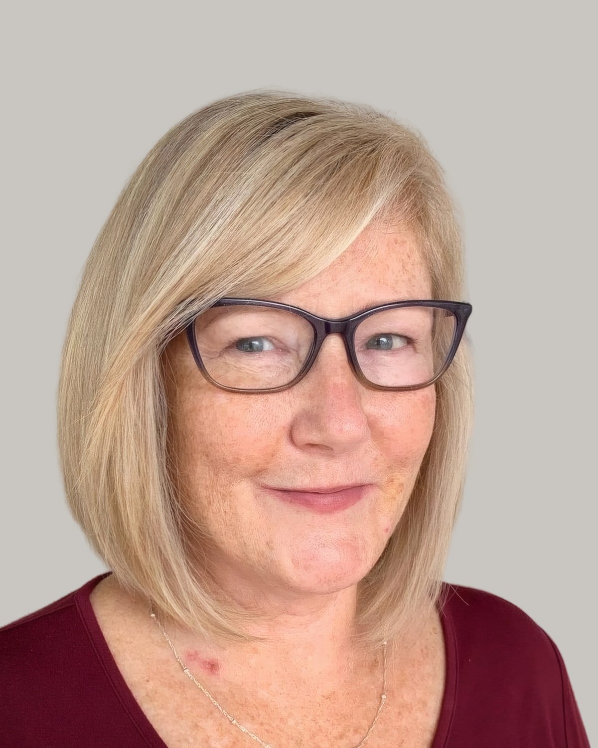 Woman with a pale blonde bob, a side part and dark rectangular glasses