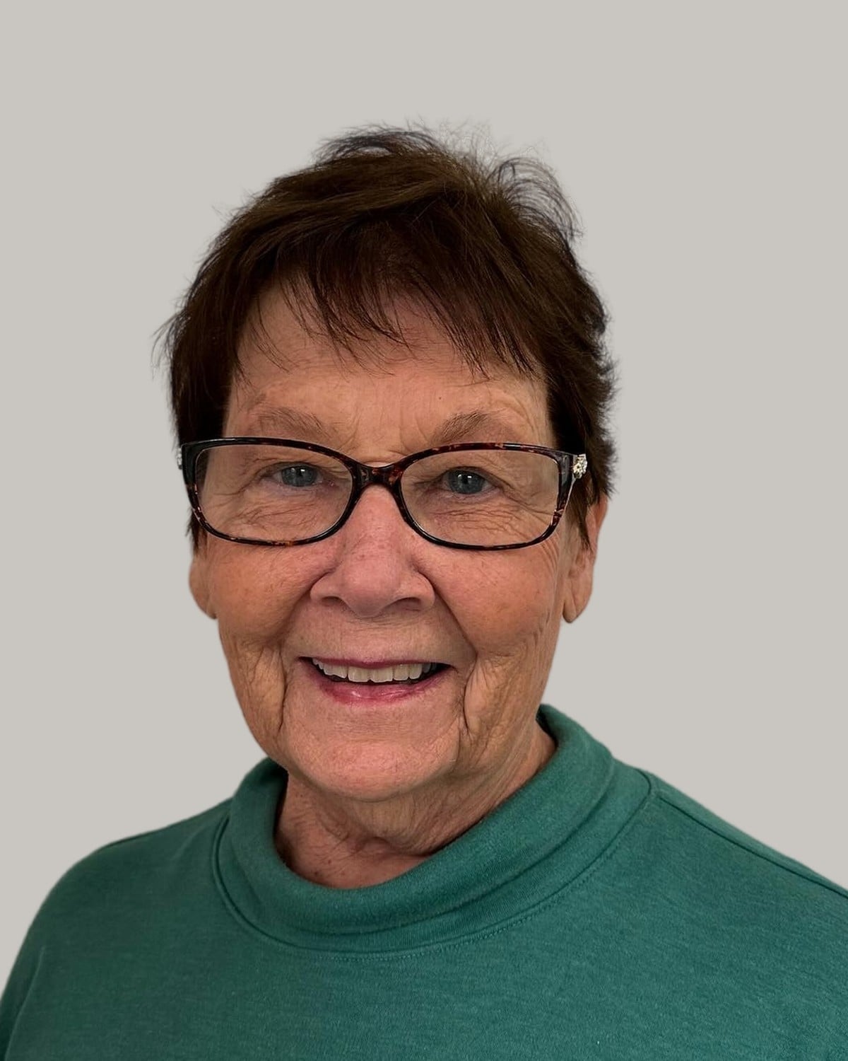 Smiling woman with a short dark crop and black glasses, in a green sweater