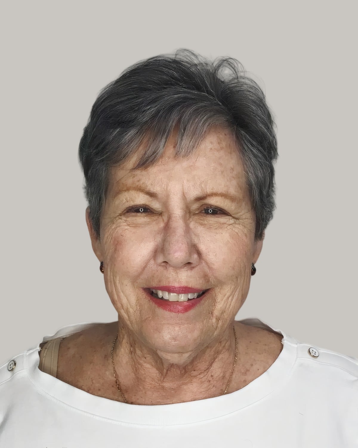Smiling woman with a short gray crop and a soft fringe, in a white top