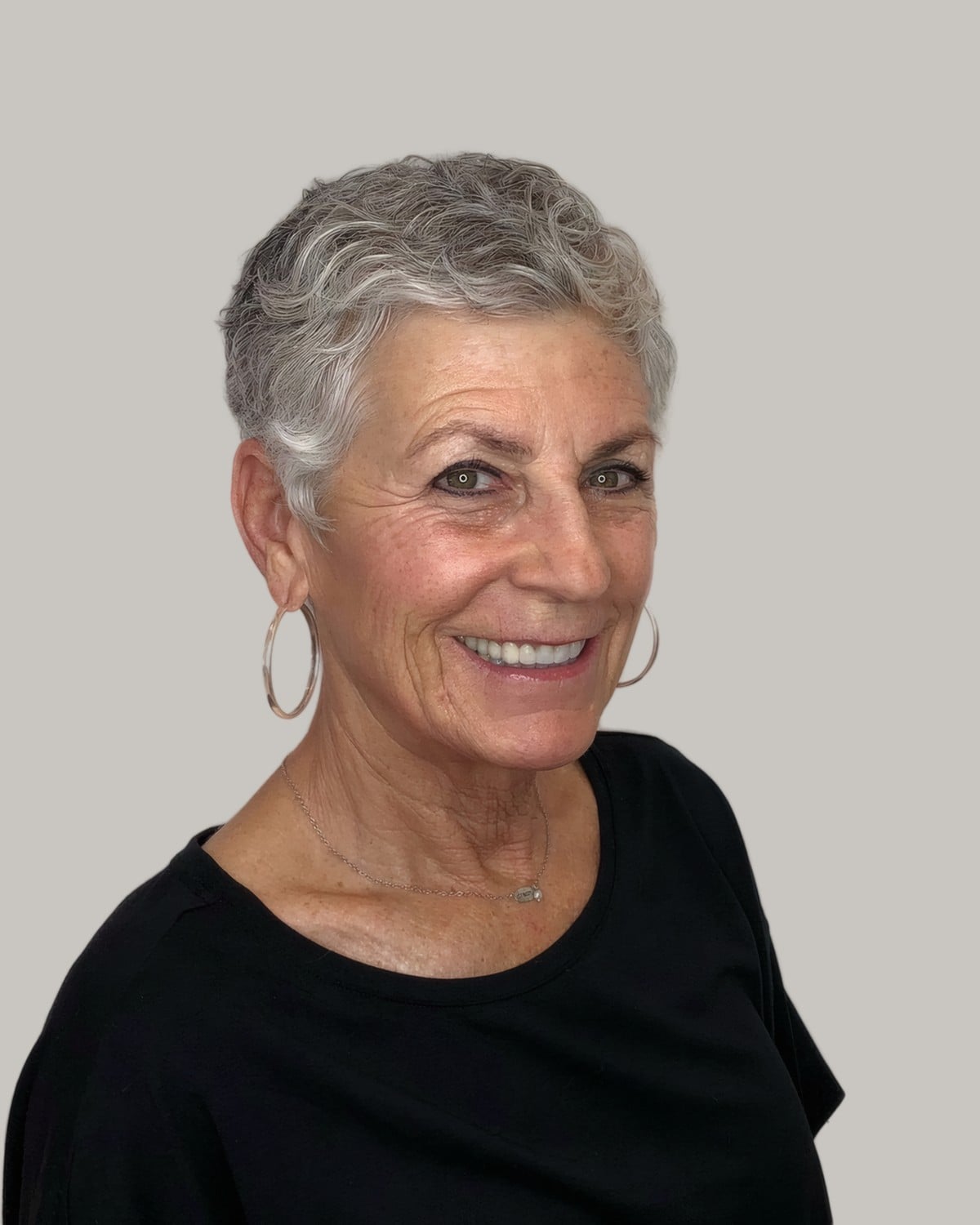 Smiling woman with a cropped silver pixie and large hoop earrings