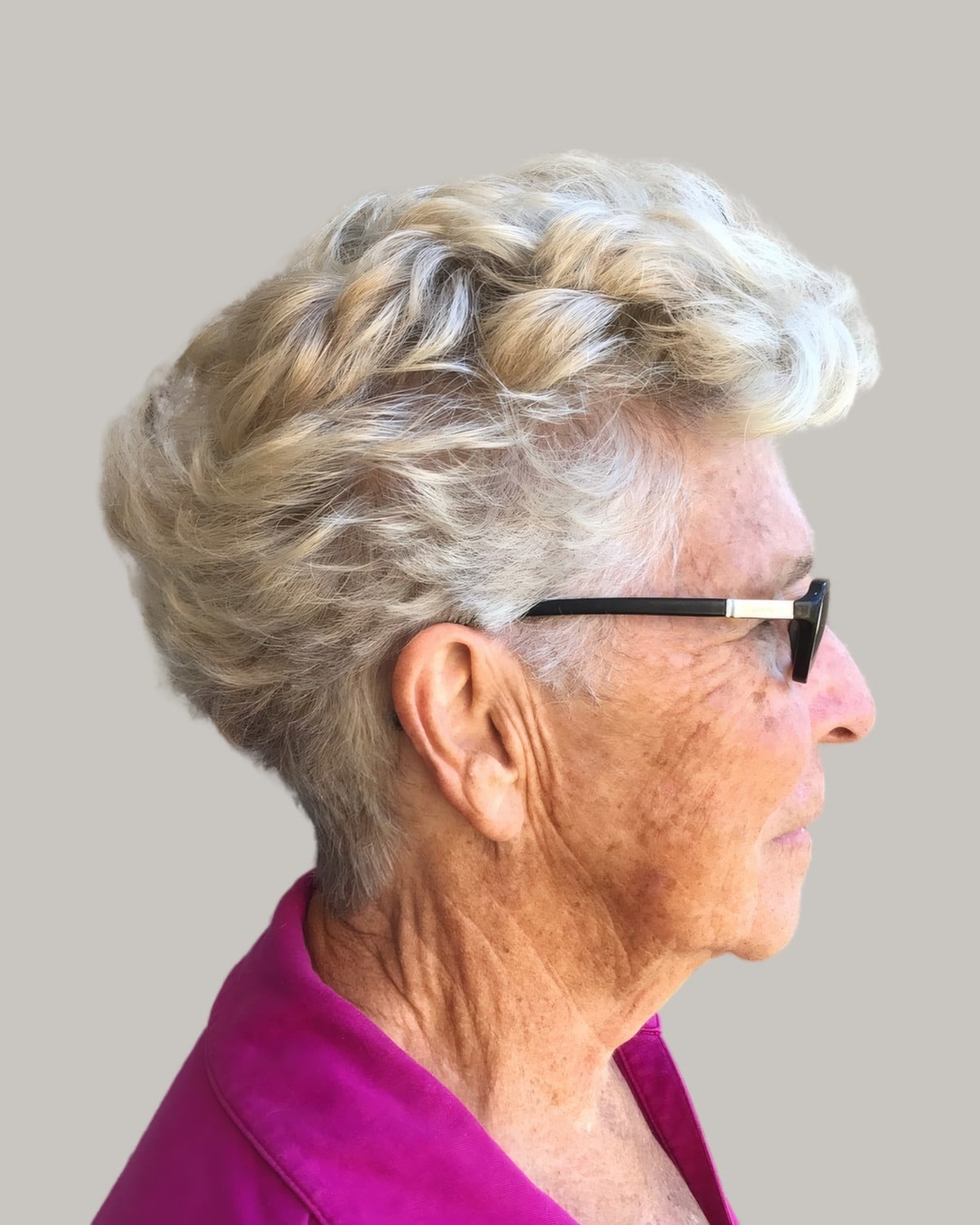 Woman with short pale blonde curls and dark glasses, seen in profile