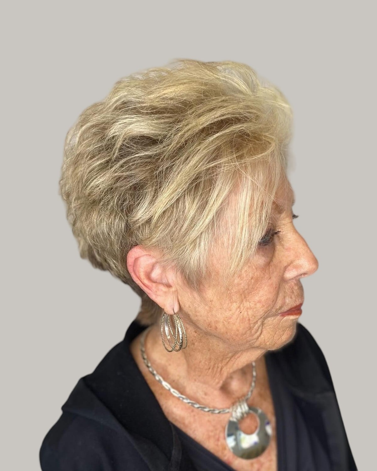 Woman with a pale blonde feathered pixie and hoop earrings, in three-quarter view