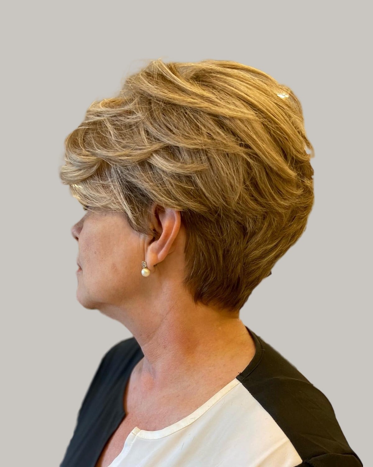 Woman with a golden-blonde feathered pixie, seen in profile